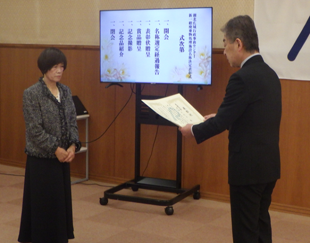 向かって左側に田中さん、右側に表彰状を読み上げている松井管理者の写真