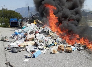 道路上でごみが実際に燃えている最中の写真。赤い炎と黒煙があがっている。