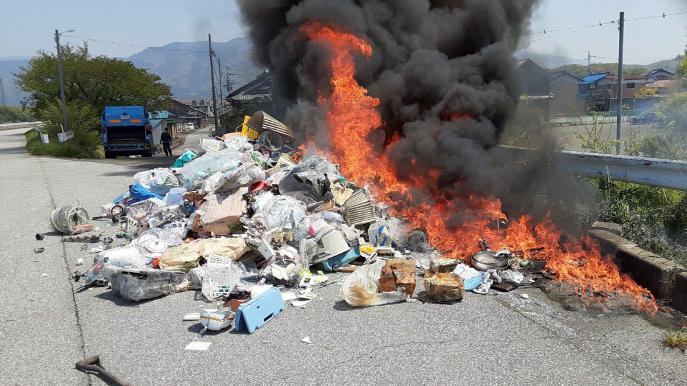 道路上でごみが実際に燃えている最中の写真。赤い炎と黒煙があがっている。